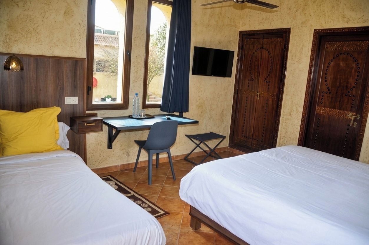 A hotel room with two beds, a desk, a chair, a TV, and a window with curtains.