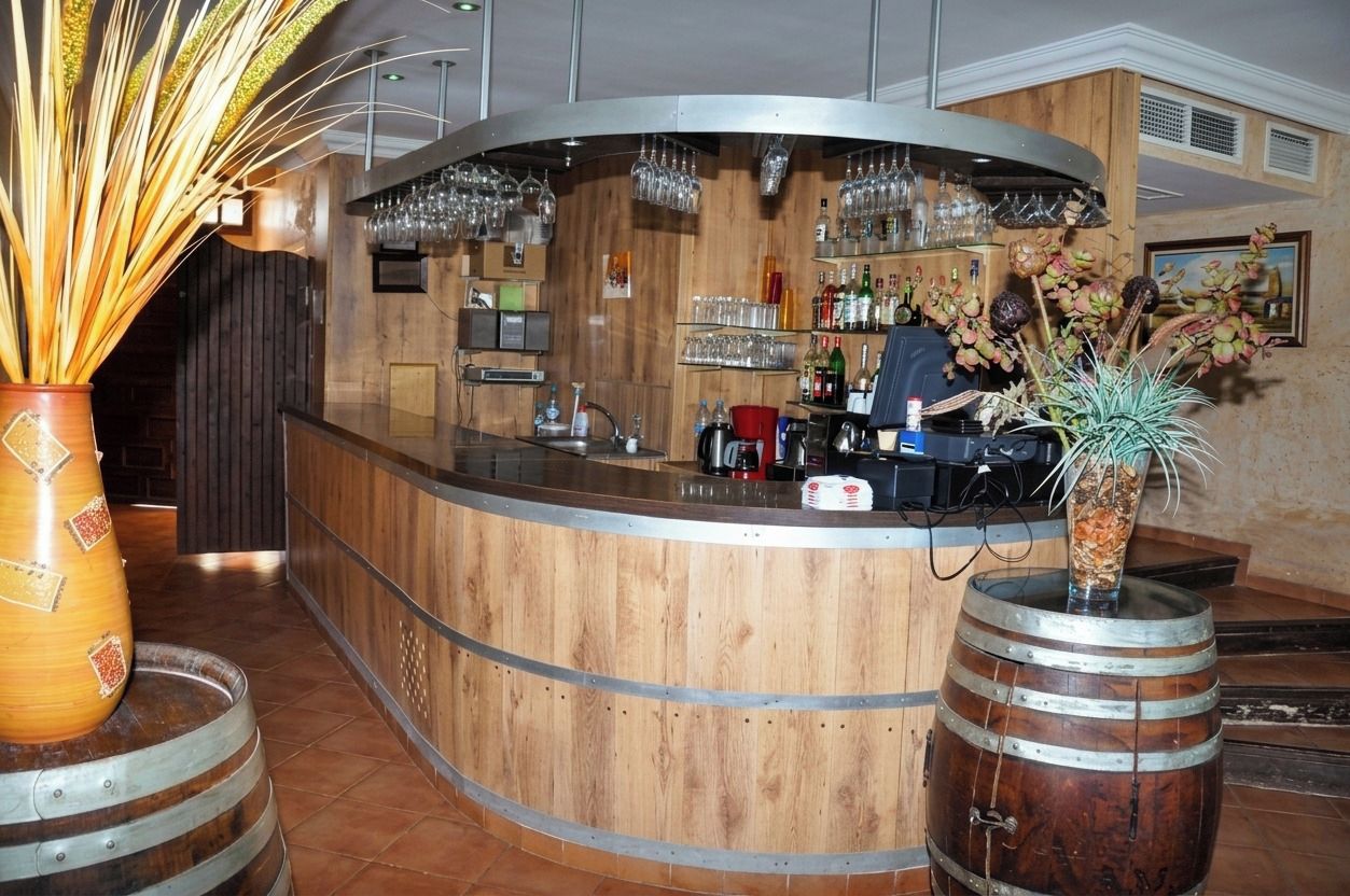 A bar area with a wooden counter, wine glasses, bottles, and a decorative plant.