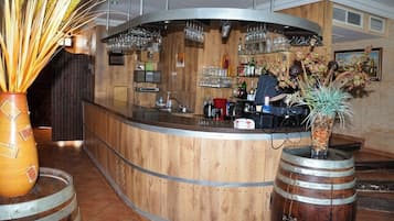 A bar area with a wooden counter, wine glasses, bottles, and a decorative plant.