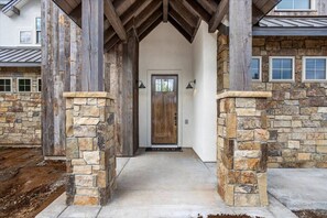 A stone-clad entrance with a wooden door and a concrete pathway leading to it. - Donnelly 4BR Home • Hot Tub • Firepit • Fireplace (McCall)