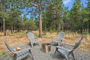 A campsite with two Adirondack chairs, a metal fire pit, and a firewood stack. - Donnelly 4BR Home • Hot Tub • Firepit • Fireplace (McCall)