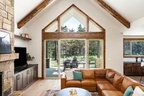 A spacious living area with a large window, a stone fireplace, and a leather sofa. - Donnelly 4BR Home • Hot Tub • Firepit • Fireplace (McCall)