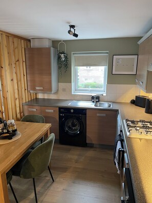 A compact kitchen with a built-in washer, a dining table with chairs, and a window providing natural light. - Luxury River Tyne | Newcastle Contractor Stay | Monday to Friday (Gateshead)
