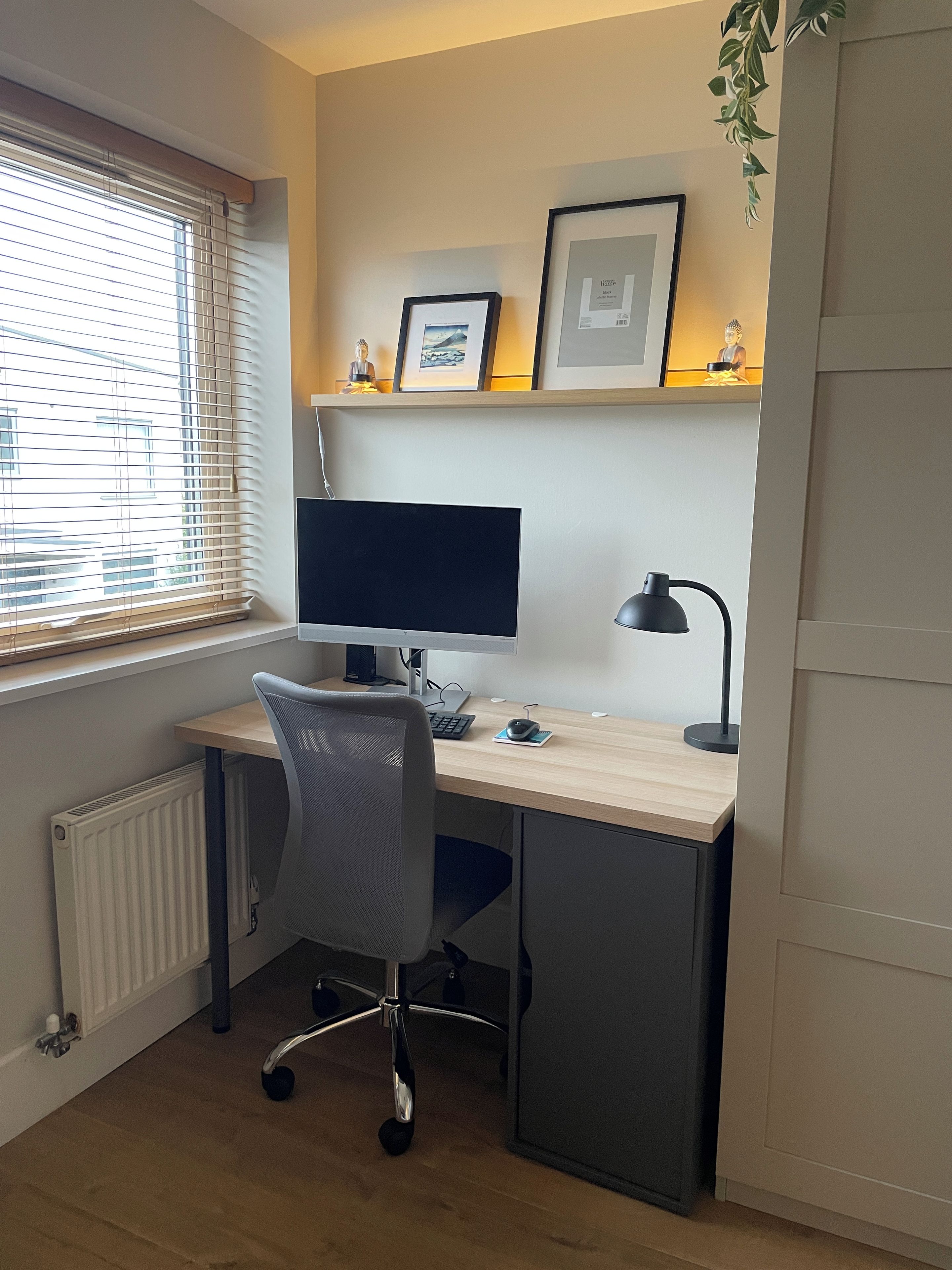 A home office setup with a desk, computer, chair, and shelving with framed pictures.