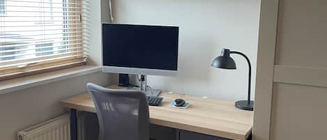 Un espacio de trabajo en casa con escritorio, computadora, silla y estanterías con fotografías enmarcadas.