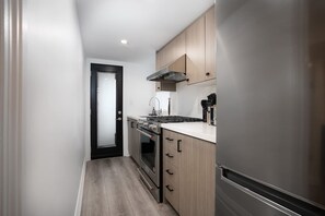 A compact kitchen with a stainless steel refrigerator, a built-in oven, a stovetop, and wooden cabinets.