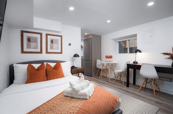 A modern hotel room with a bed, a desk, and a dining area. - Sun-Drenched West End Retreat | Walk to High Park (Toronto)
