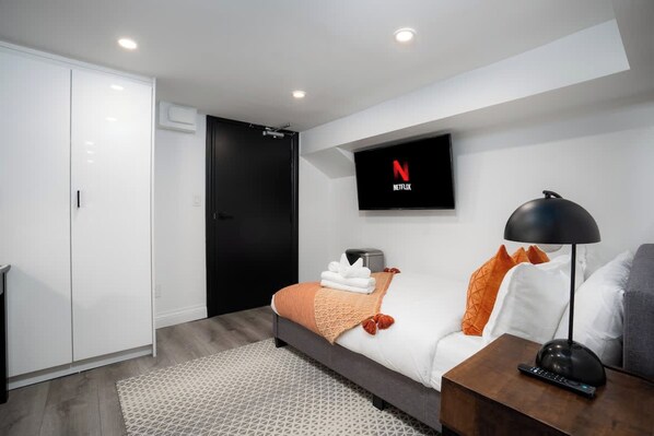 A modern hotel room with a bed, a TV mounted on the wall, a wardrobe, and a bedside table with a lamp.