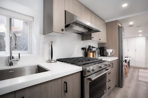 A modern kitchen with a stainless steel sink, a gas stove, and a built-in oven. - Sun-Drenched West End Retreat | Walk to High Park (Toronto)