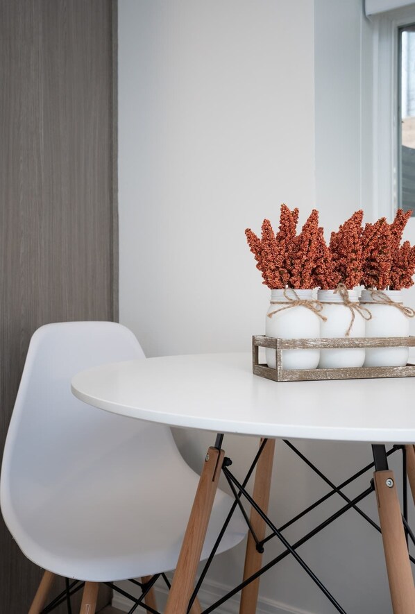 Une table blanche sur laquelle est posée une caisse en bois contenant des œufs blancs et des feuilles rouges. La table est placée sur une chaise blanche aux pieds en bois.