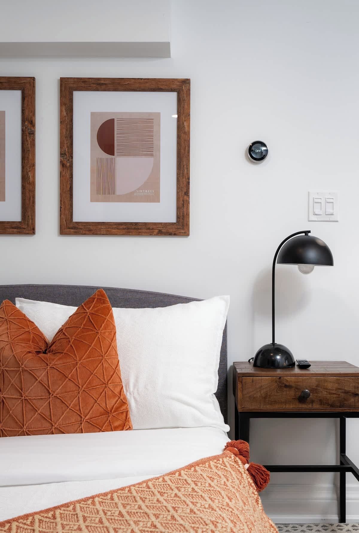 A neatly made bed with two pillows, a bedside table with a lamp, and two framed pictures on the wall.