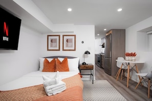 A hotel room with a bed, a desk, a chair, a TV, and a kitchenette. - Sun-Drenched West End Retreat | Walk to High Park (Toronto)