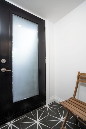 A black door with a frosted glass panel, a wooden chair, and a geometric patterned floor.