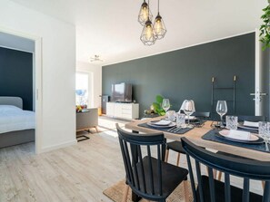 A modern dining area with a dark wall, a wooden table, and black chairs. - Utholm 1 Dike hut (St. Peter-Ording)