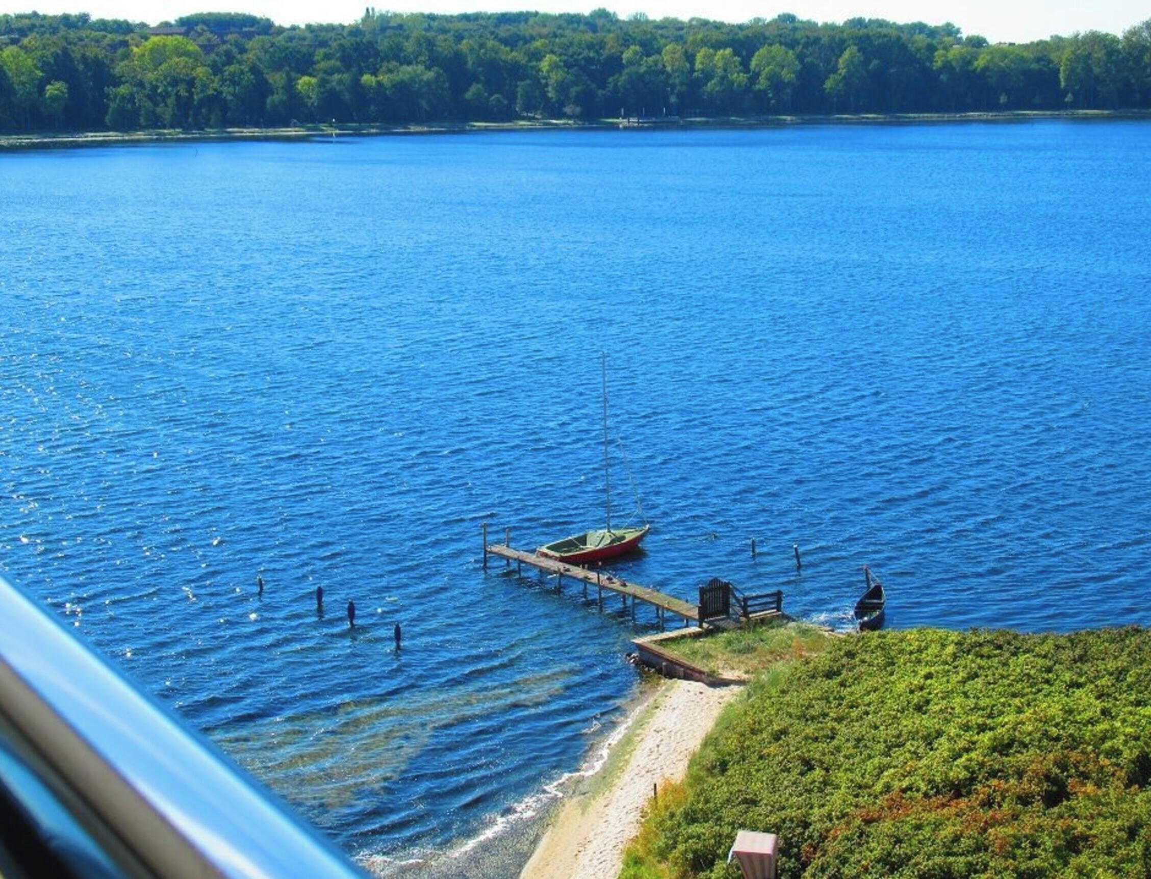 Ein See mit einem Steg, der ins Wasser ragt, umgeben von viel Grün.