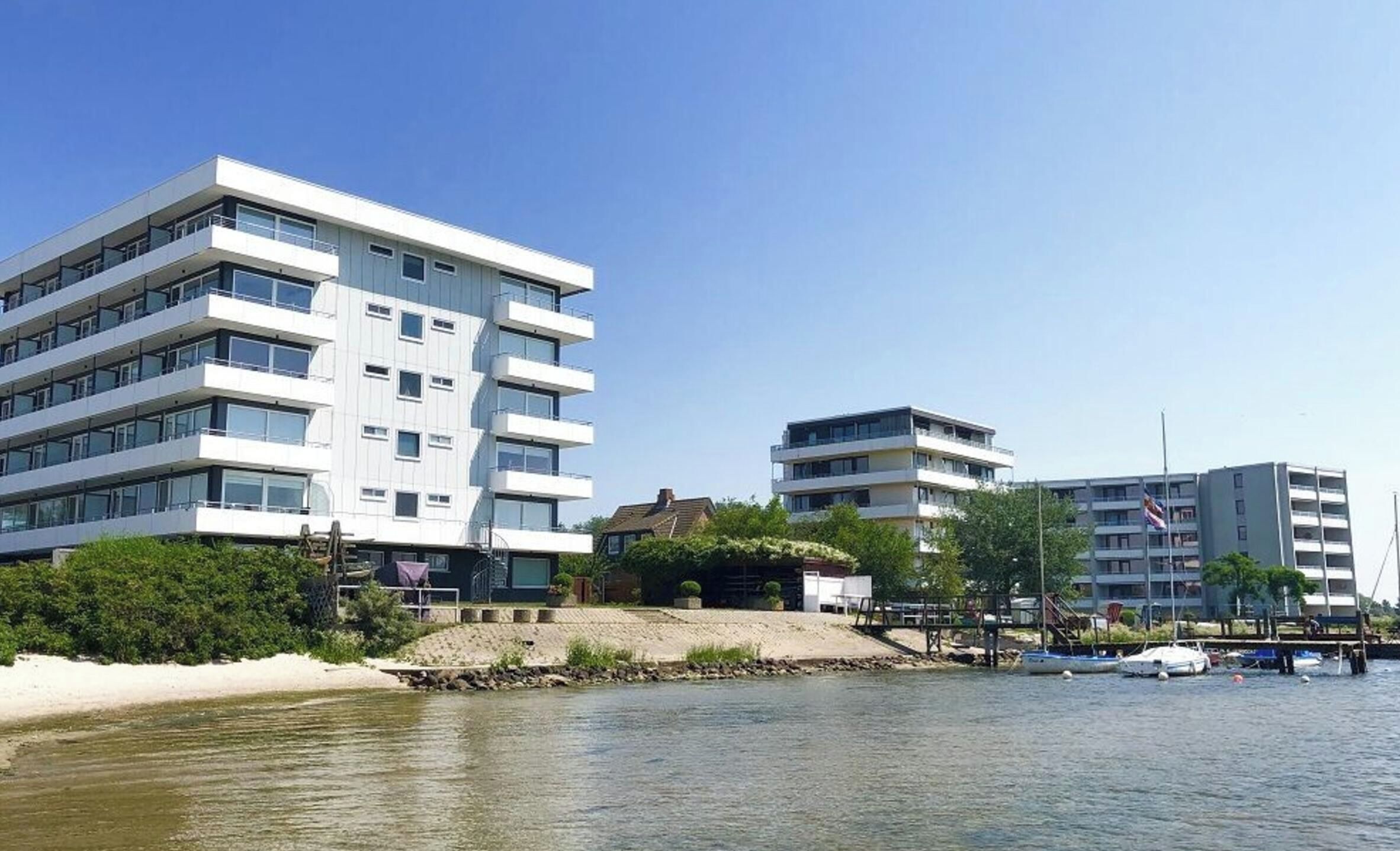 A waterfront property with modern multi-story buildings, a dock, and boats.