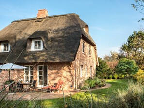 A brick house with a thatched roof, a patio with outdoor furniture, and a well-maintained garden. - Holiday Home With 1 Bedroom (St. Peter-Ording)