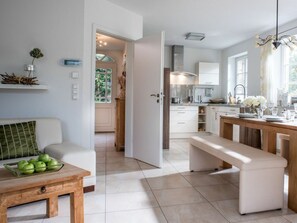 A modern kitchen with white cabinets, a wooden bench, and a dining table set for four. - Holiday Home With 1 Bedroom (St. Peter-Ording)
