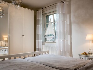 A bedroom with a bed, a window with a view, a mirror, and a bedside table with a lamp. - Holiday Home With 1 Bedroom (St. Peter-Ording)
