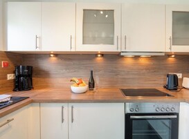 A modern kitchen with white cabinets, a wooden countertop, a coffee maker, a bowl of fruit, and a built-in oven.