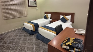 Ein Hotelzimmer mit zwei Einzelbetten, einem Schreibtisch mit Telefon und einem gemusterten Teppich.