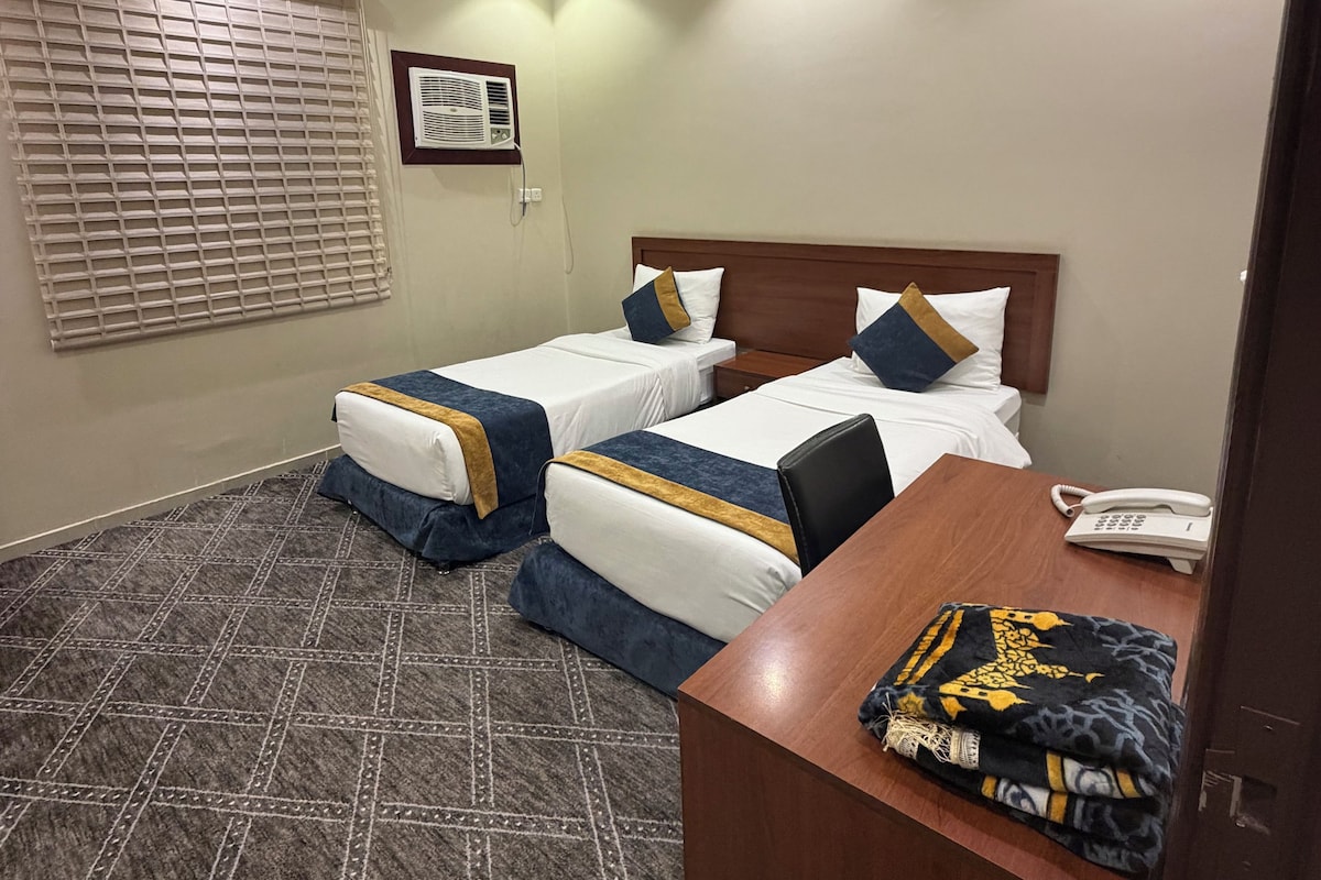 A hotel room with two single beds, a desk with a telephone, and a patterned carpet.