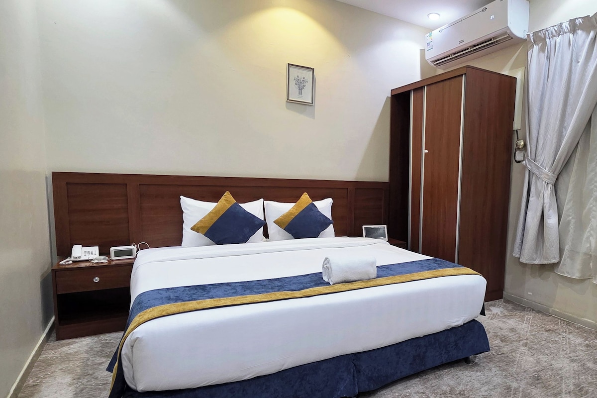 A hotel room with a bed, bedside table, and an air conditioning unit.