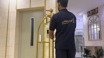 Una persona empenyent un carro d'elevaació daurat en un vestíbul d'hotel amb terres de marbre i una porta amb ratlla vertical.