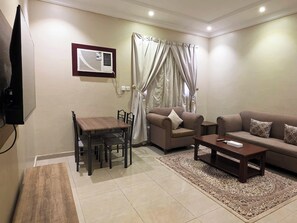 A living room with a sofa, armchair, coffee table, and a dining table with chairs.