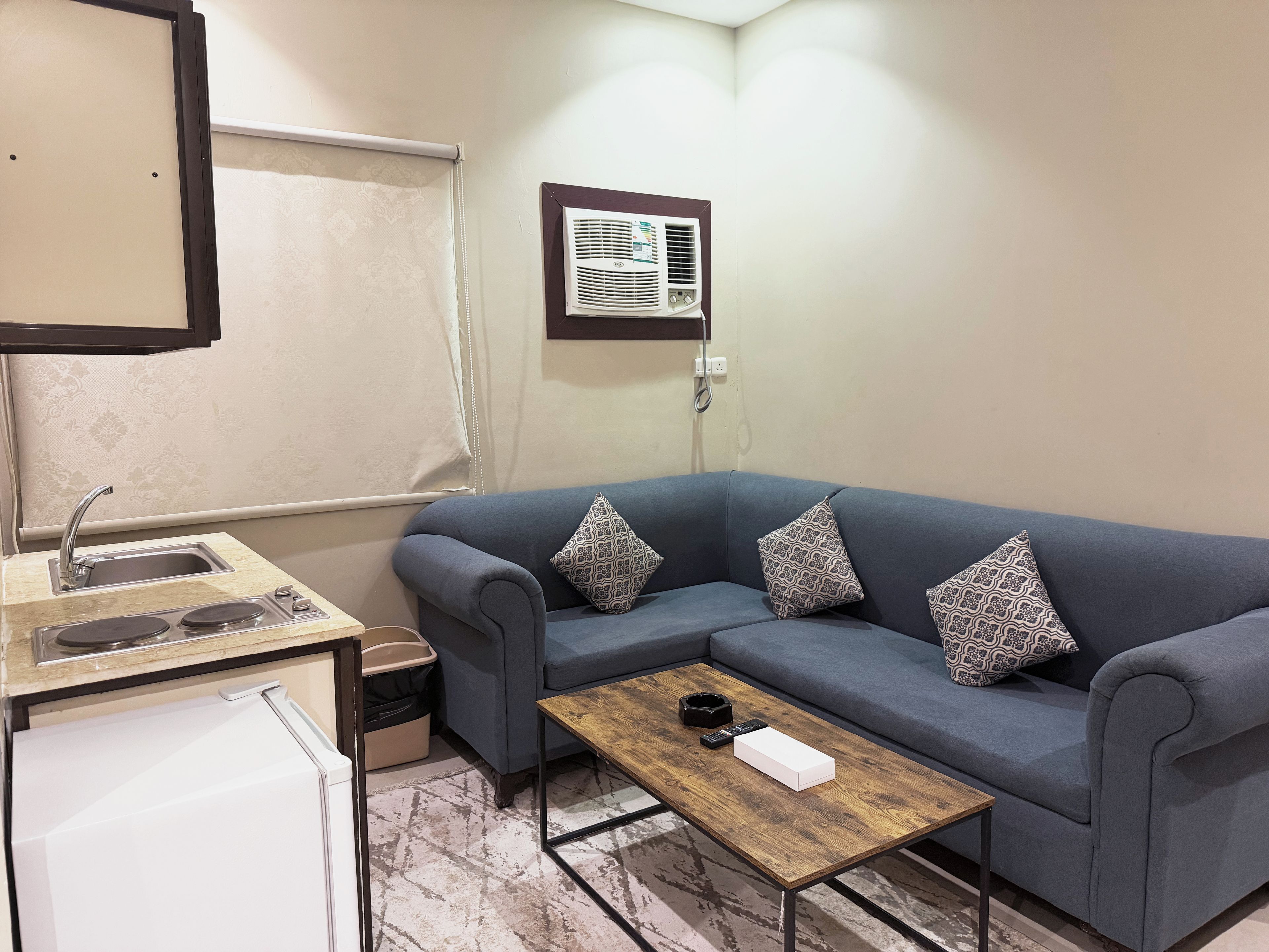 A compact living space with a kitchenette, a sofa with patterned cushions, and a small wooden table.