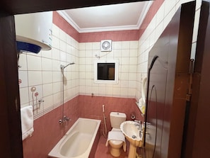A bathroom with a bathtub, toilet, sink, and a window. - High Selection Serviced Apartments (Madinah)
