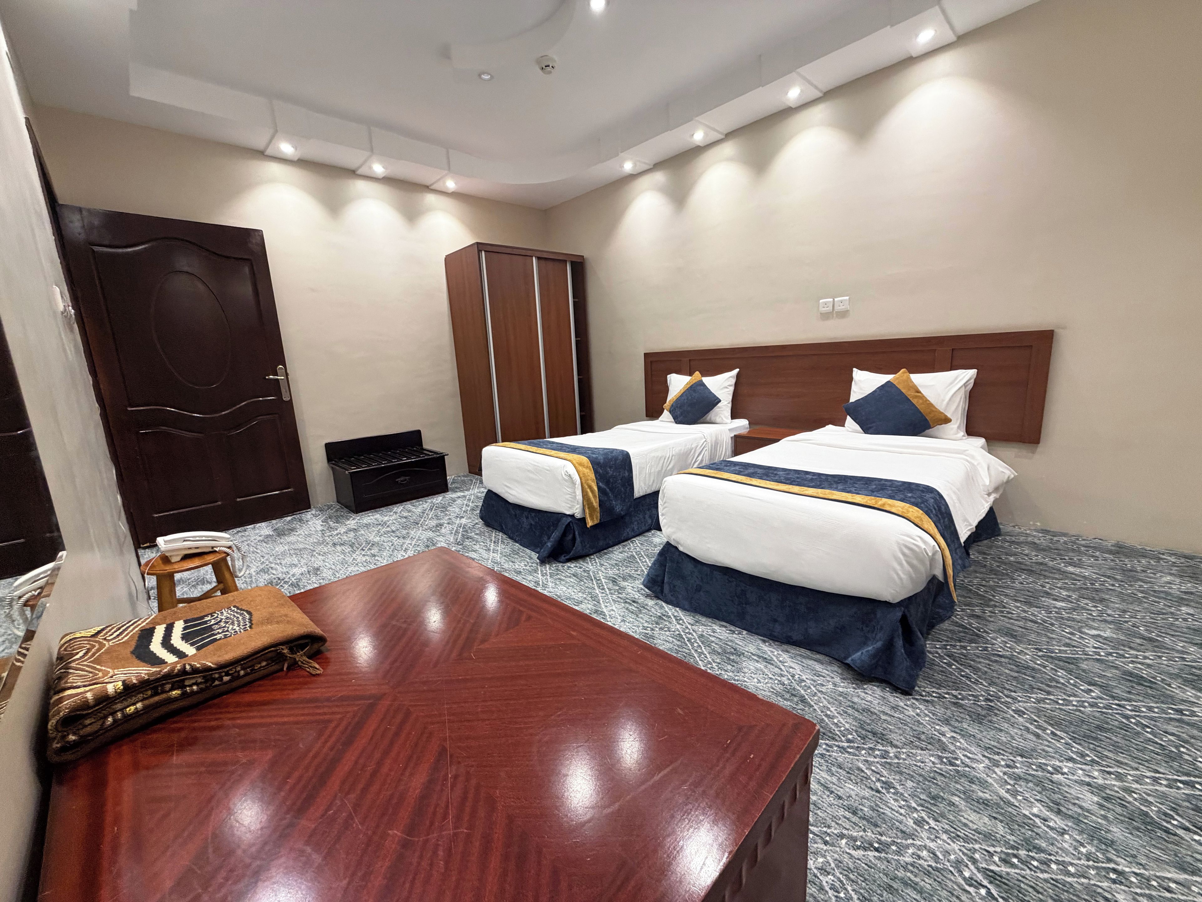 Une chambre d’hôtel avec deux lits, un bureau en bois, une armoire et un petit tabouret.
