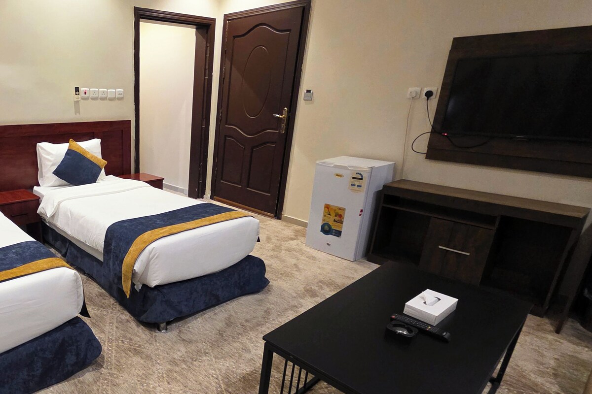A hotel room with two beds, a television, a minibar, and a fireplace.
