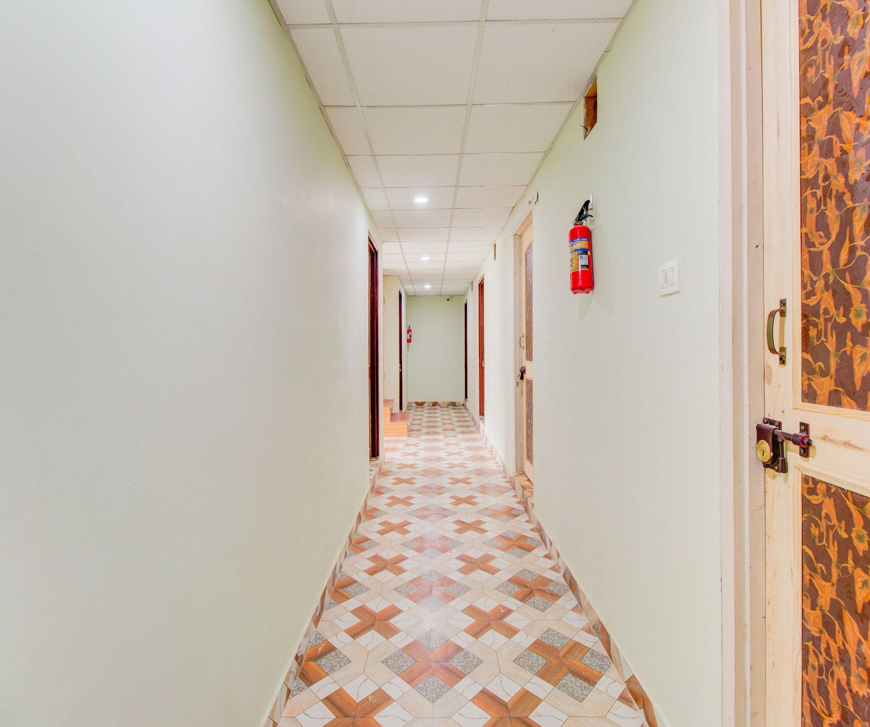 A hallway with patterned flooring, a fire extinguisher mounted on the wall, and a door with a decorative panel.