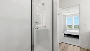 Een moderne badkamer met een douchecabine van glas, een zichtbare douchekop en een groot raam met uitzicht op de omgeving.