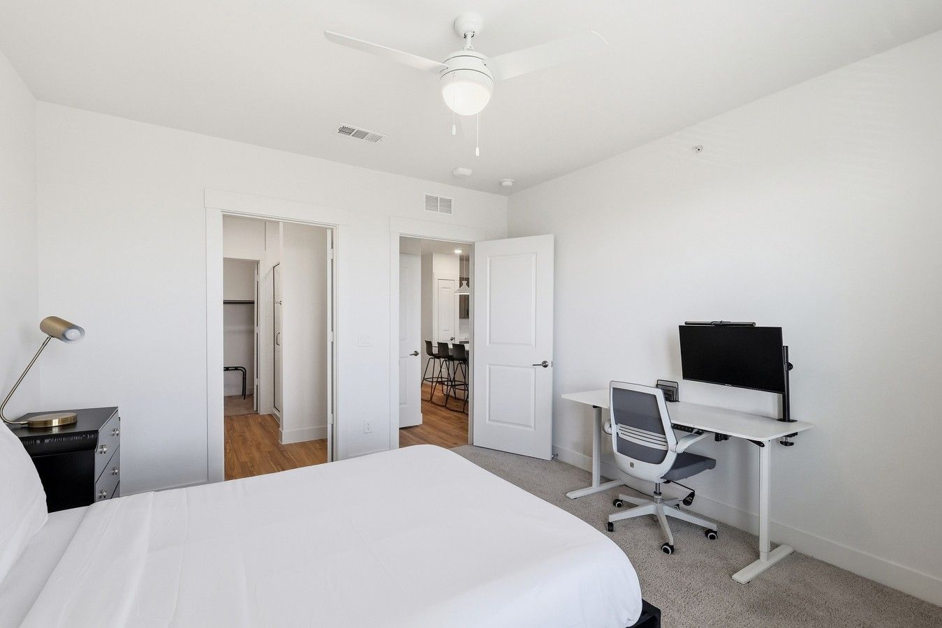 A bedroom with a bed, a desk with a computer, and a ceiling fan.