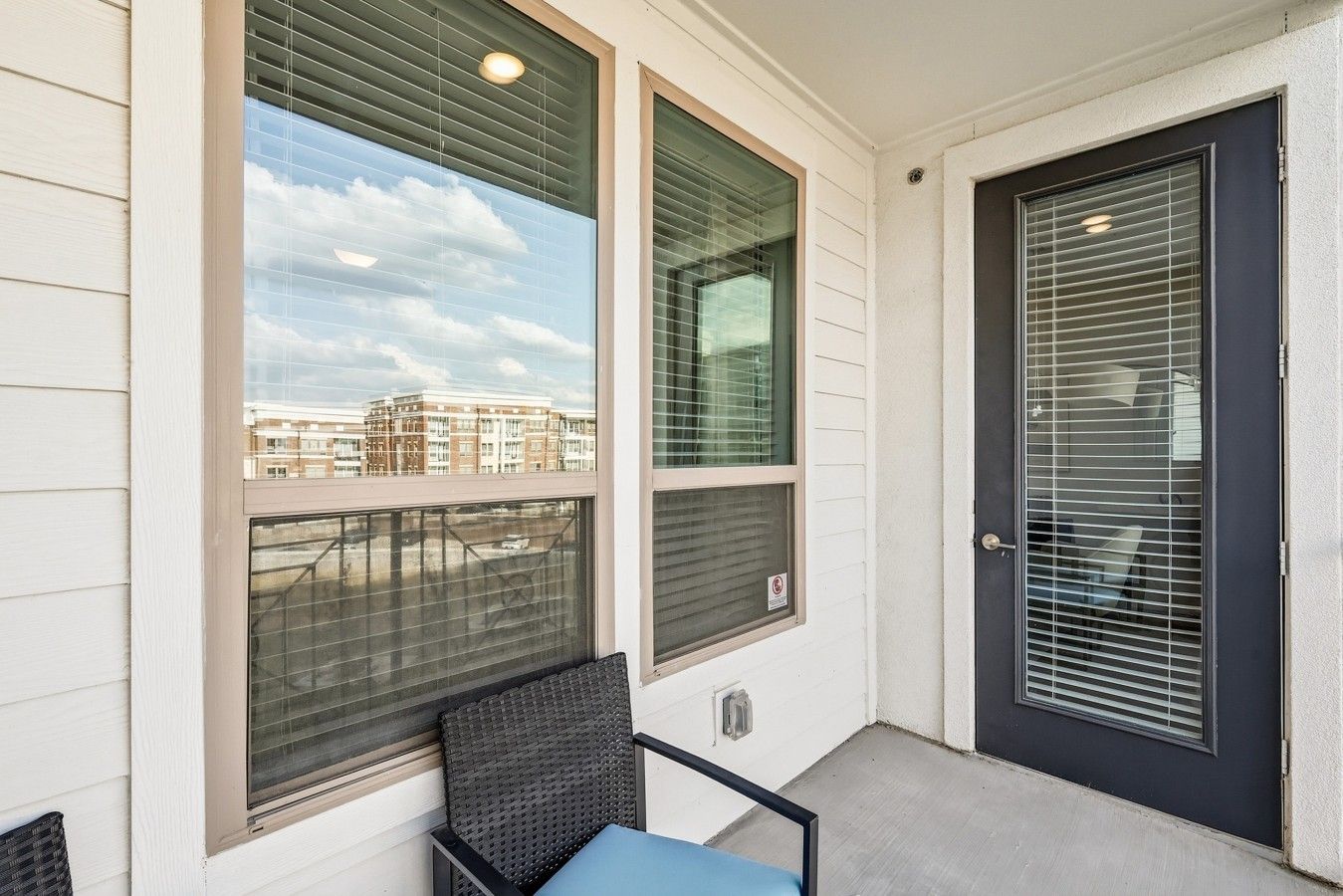 Un balcon avec une chaise et une table, une porte et des fenêtres équipées de stores.