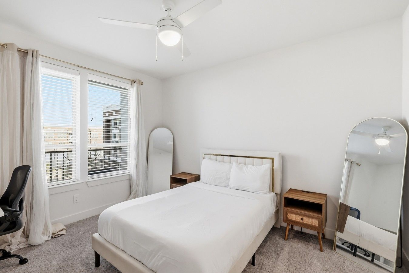 Une chambre d’hôtel équipée d’un lit, d’un bureau, d’une chaise, d’un ventilateur de plafond et d’une grande fenêtre avec des stores.