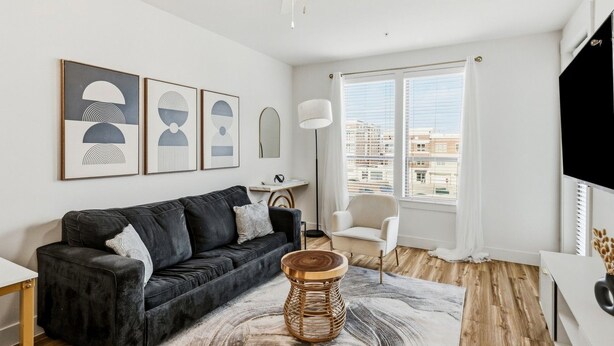 En moderne stue med en sort sofa, en hvid lænestol, en gulvlampe og billedkunst på væggen.