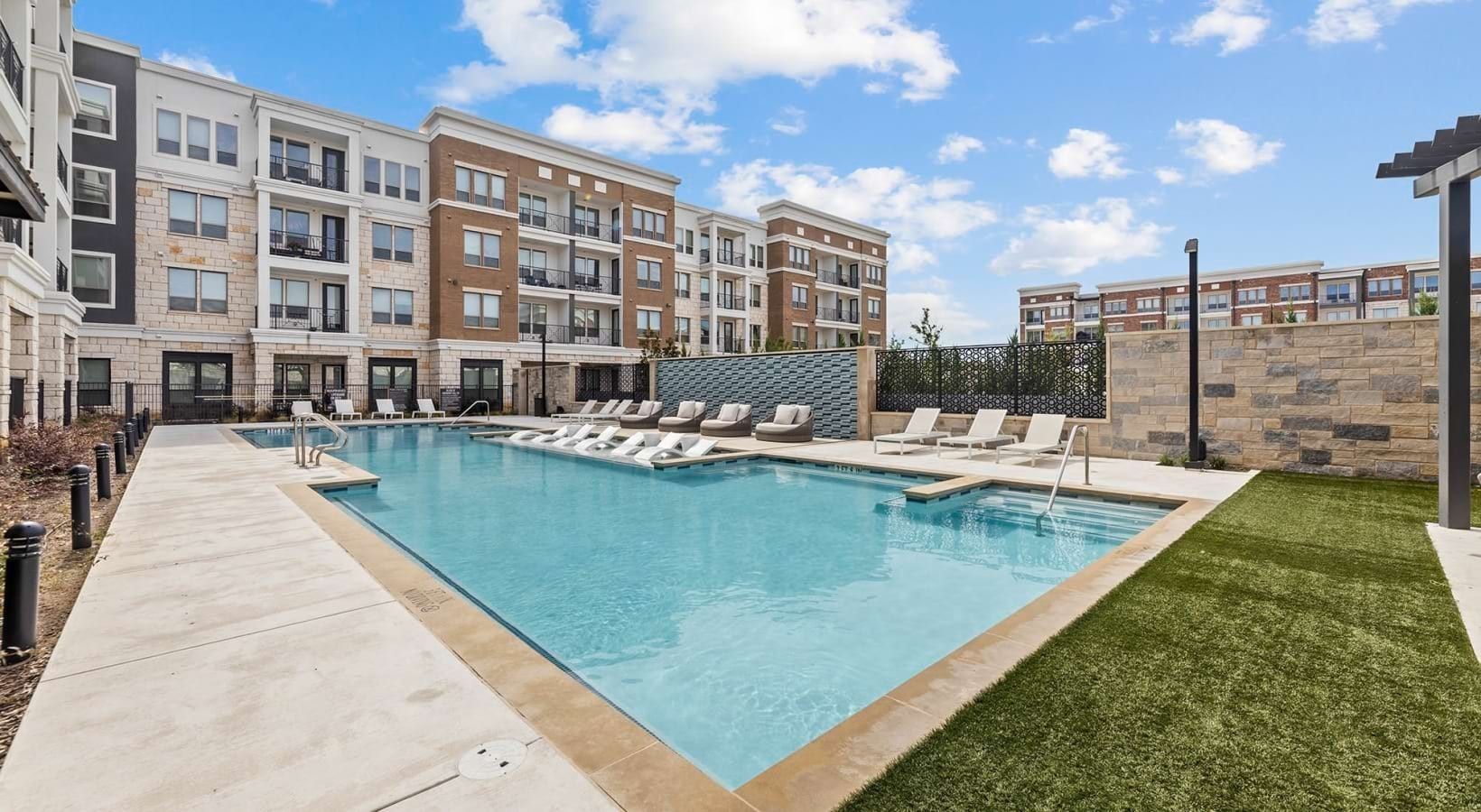 A swimming pool with lounge chairs, a paved walkway, and a building with multiple balconies.