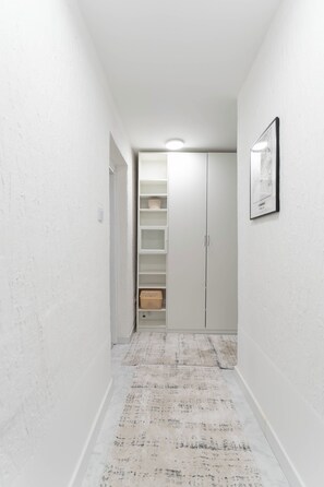 A narrow hallway with white walls, a patterned rug, and a closet with open doors. - BeoVibe Studio Belgrade (Beograd)