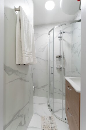 A modern bathroom with a glass shower enclosure, a marble-tiled wall, and a white towel hanging on a metal towel rack. - BeoVibe Studio Belgrade (Beograd)