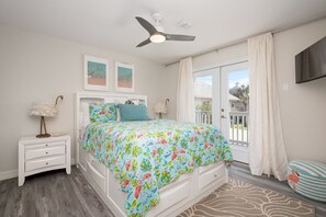 A bedroom with a bed, a nightstand, a ceiling fan, a window with curtains, and a view of the outside. - Casa de Cielos Azure - Waterfront, Dock, Pools (Port Isabel)