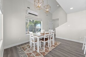 A dining area with a wooden table and white chairs, a patterned rug, and a window with blinds. - Casa de Cielos Azure - Waterfront, Dock, Pools (Port Isabel)