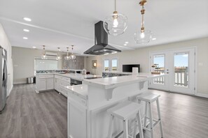 A modern kitchen with white cabinetry, a central island with stools, pendant lighting, and a view to the outside. - Casa de Cielos Azure - Waterfront, Dock, Pools (Port Isabel)