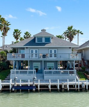 A two-story waterfront house with a balcony, dock, and palm trees in the background. - Casa de Cielos Azure - Waterfront, Dock, Pools (Port Isabel)
