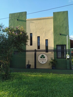 Ein Gebäude mit grüner Fassade, einem verschlossenen Eingang und einem Logo mit einem Baum und dem Text 'YVYRA Alojamiento Iguaçu'.