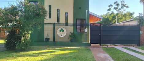 Una propiedad con acceso restringido, fachada verde y beige, un logotipo con un árbol y un camino de entrada pavimentado.