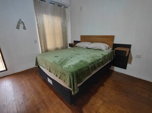 A bedroom with a wooden bed, a green bedspread, a nightstand, and a window with curtains. - Delightful 1-bedroom apartment with AC in Puerto Iguazú (Puerto Iguazú)