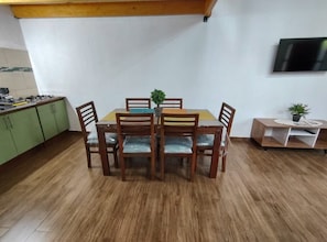 Ein Essbereich mit Holztisch und -stühlen, einem kleinen Topfpflanzen und einem an der Wand befestigten Fernseher.